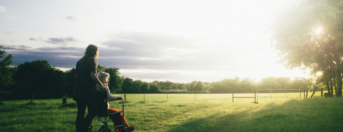 Pushing an elderly woman in a wheelchair in a meadow